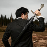 Man in a black suit holding a sword against a forest background